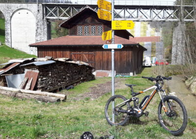 Bergamont E Bike MTB Fully vor Wanderwegweiser, Bach und Eisenbrücke