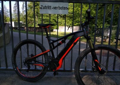 Rot schwarzes E Bike vor Gittertor mit Schild Zutritt verboten
